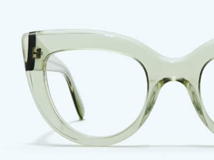 Close-up of a translucent green cat-eye eyeglass frame, showcasing the thick acetate material and subtle glossy finish against a pale background.